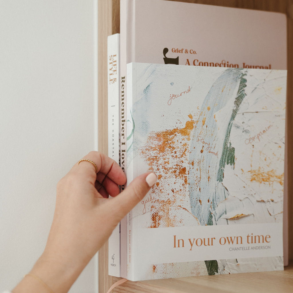 Hand placing a book titled 'In your own time - guided grief journal' on a shelf.